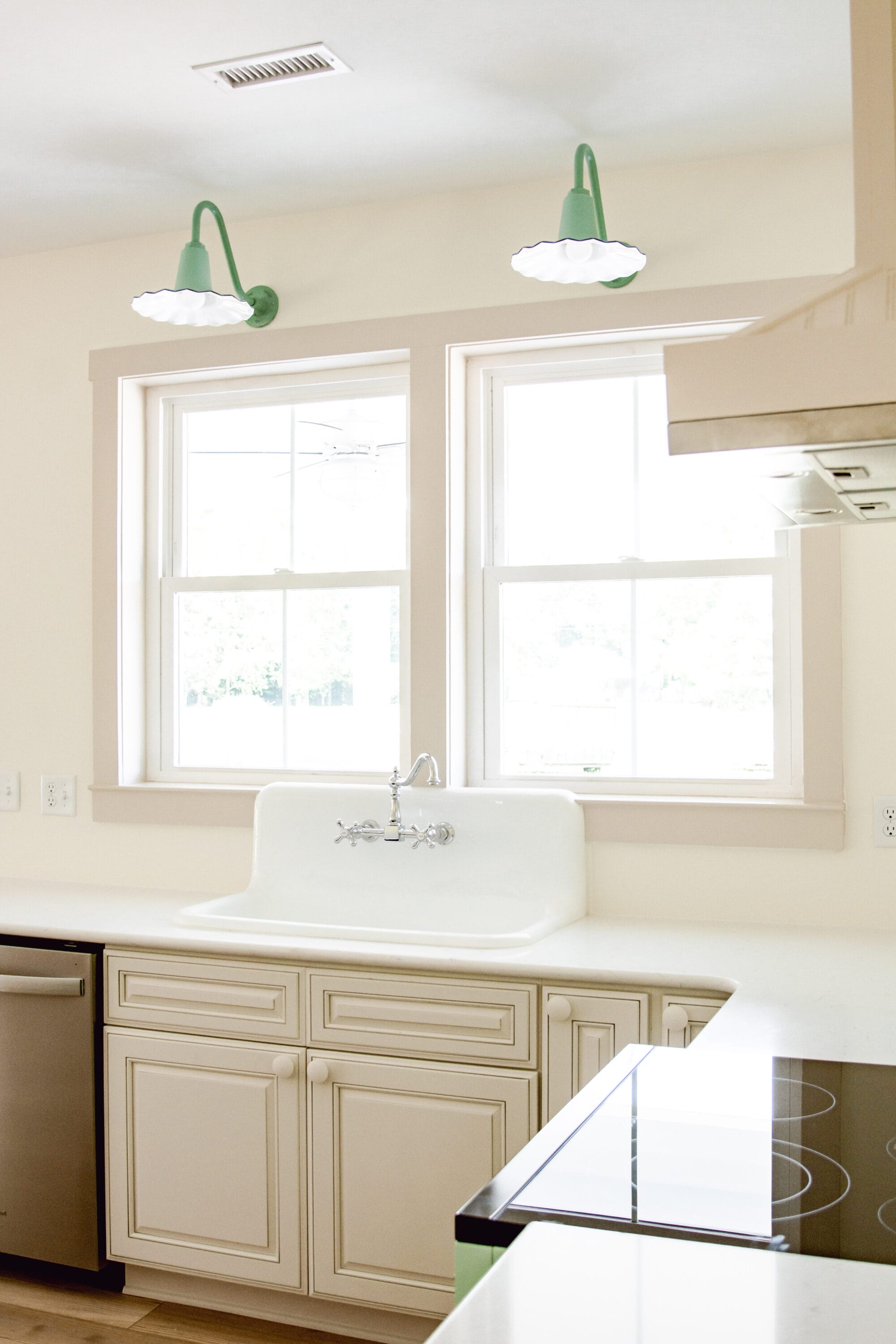 high back kitchen sink with 2 double windows above it and 2 jadeite green sconce lights over the windows