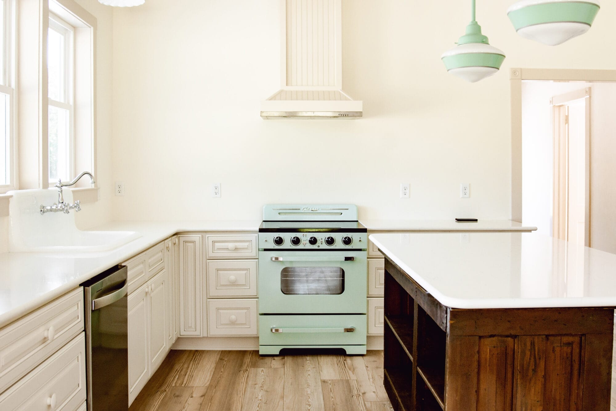 white cottage kitchen with retro mint green stove and schoolhouse lights over the island