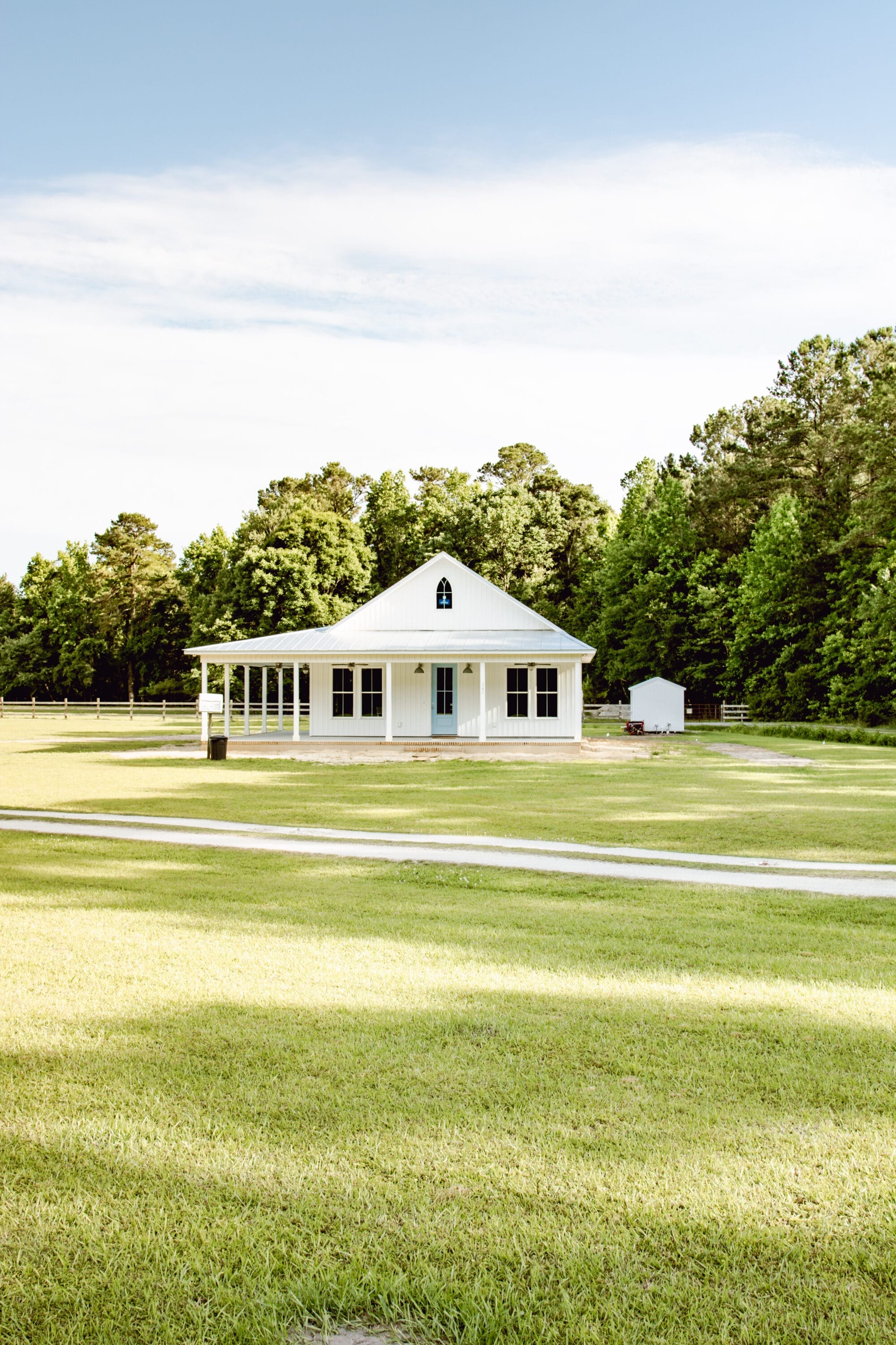 new-old cottage with white vertical siding, a metal roof, a blue door, a Carpenter Gothic pointed window, and a gravel driveway