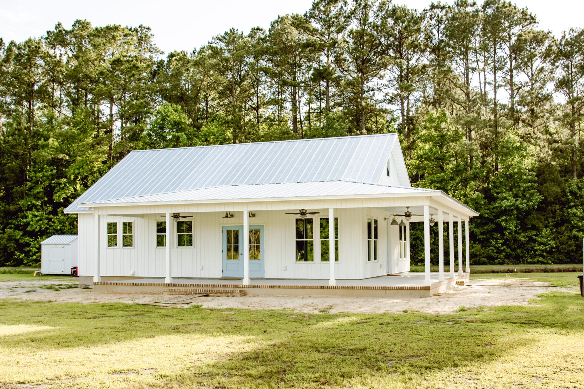 country cottage with white vertical siding, metal roof, blue doors, and a wraparound porch
