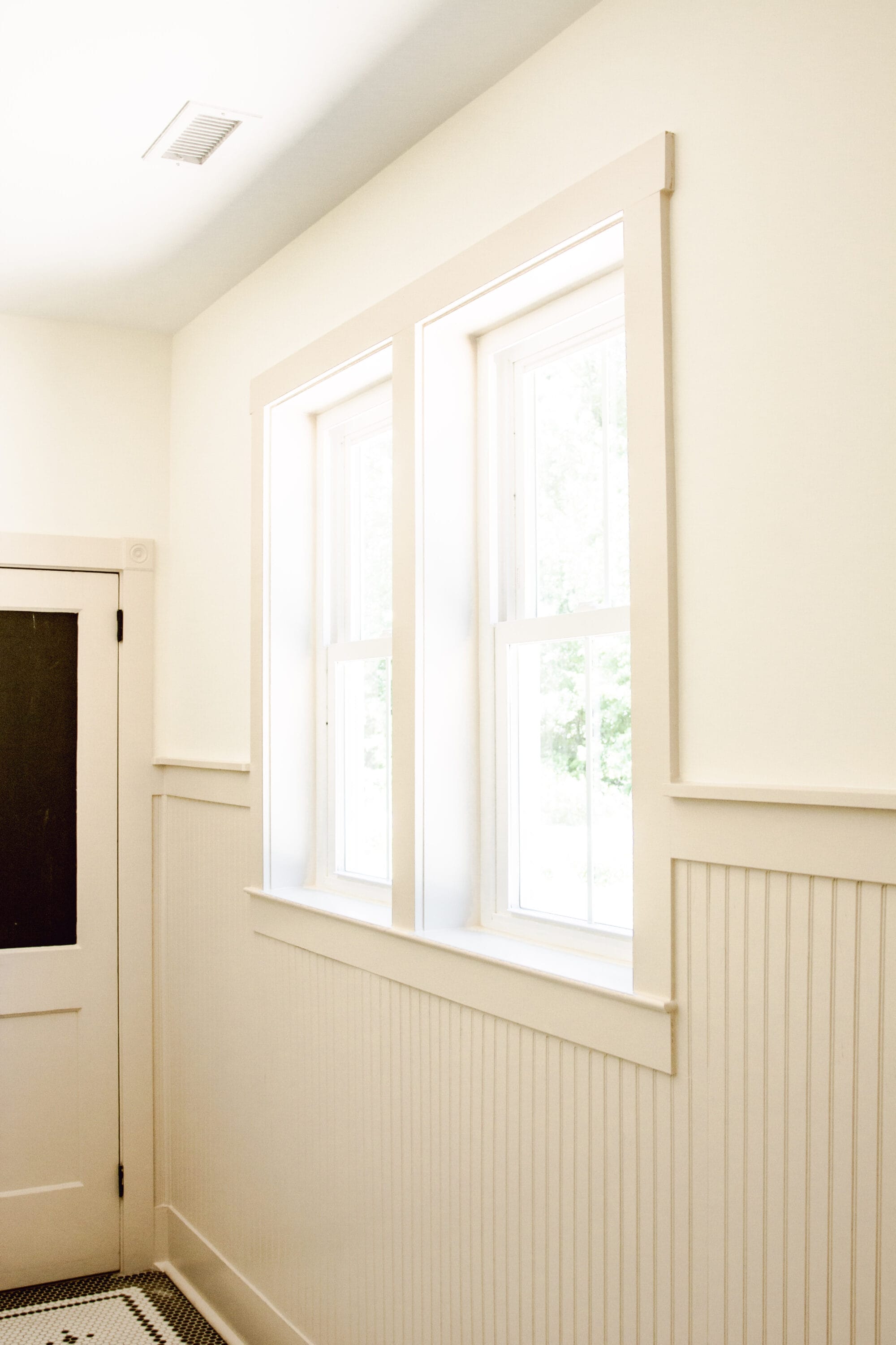 double windows and tan beadboard walls inside a cottage bathroom