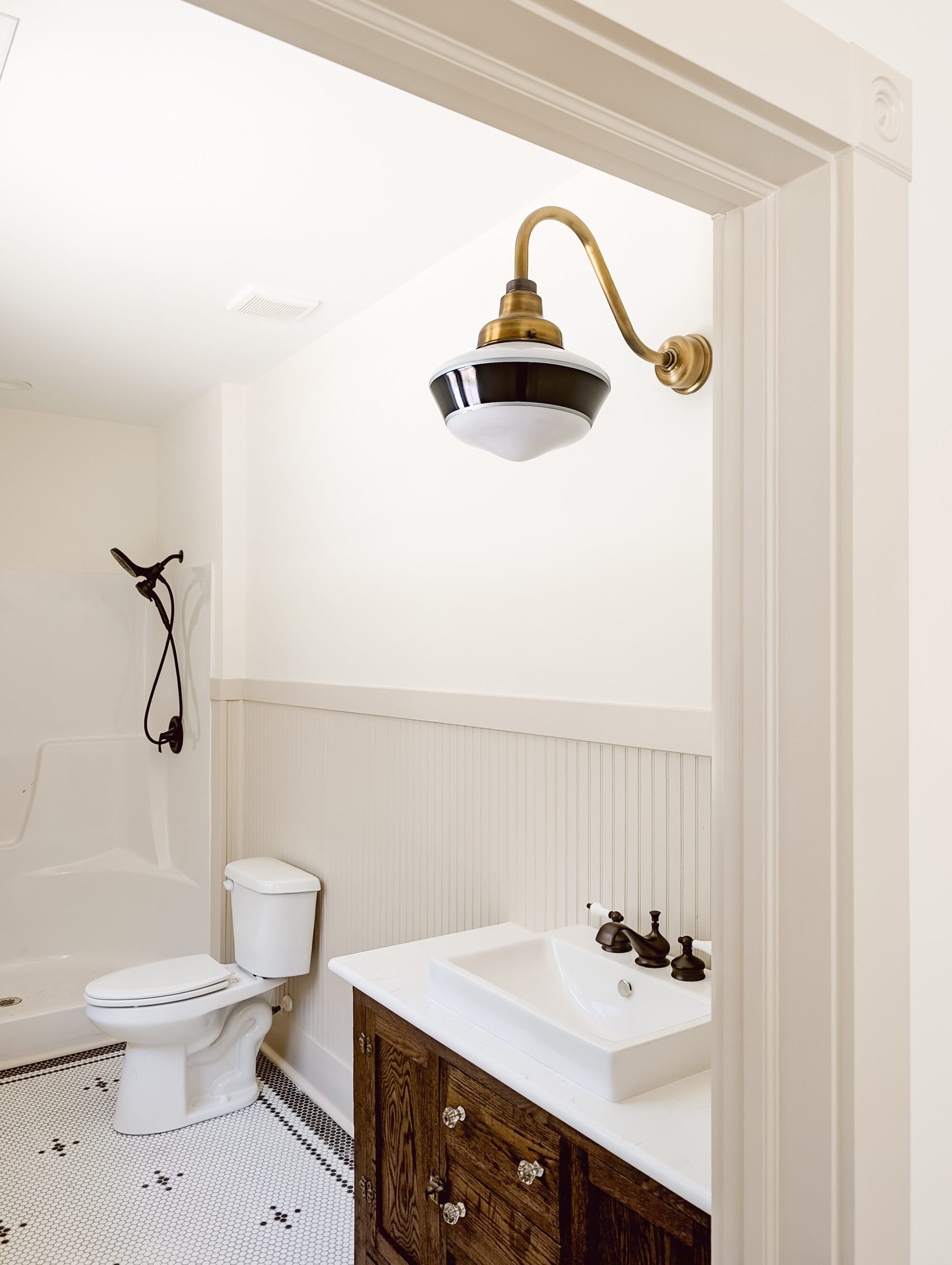 new old cottage primary bathroom with black and white details, white walls, tan beadboard paneling, and an antique bathroom vanity