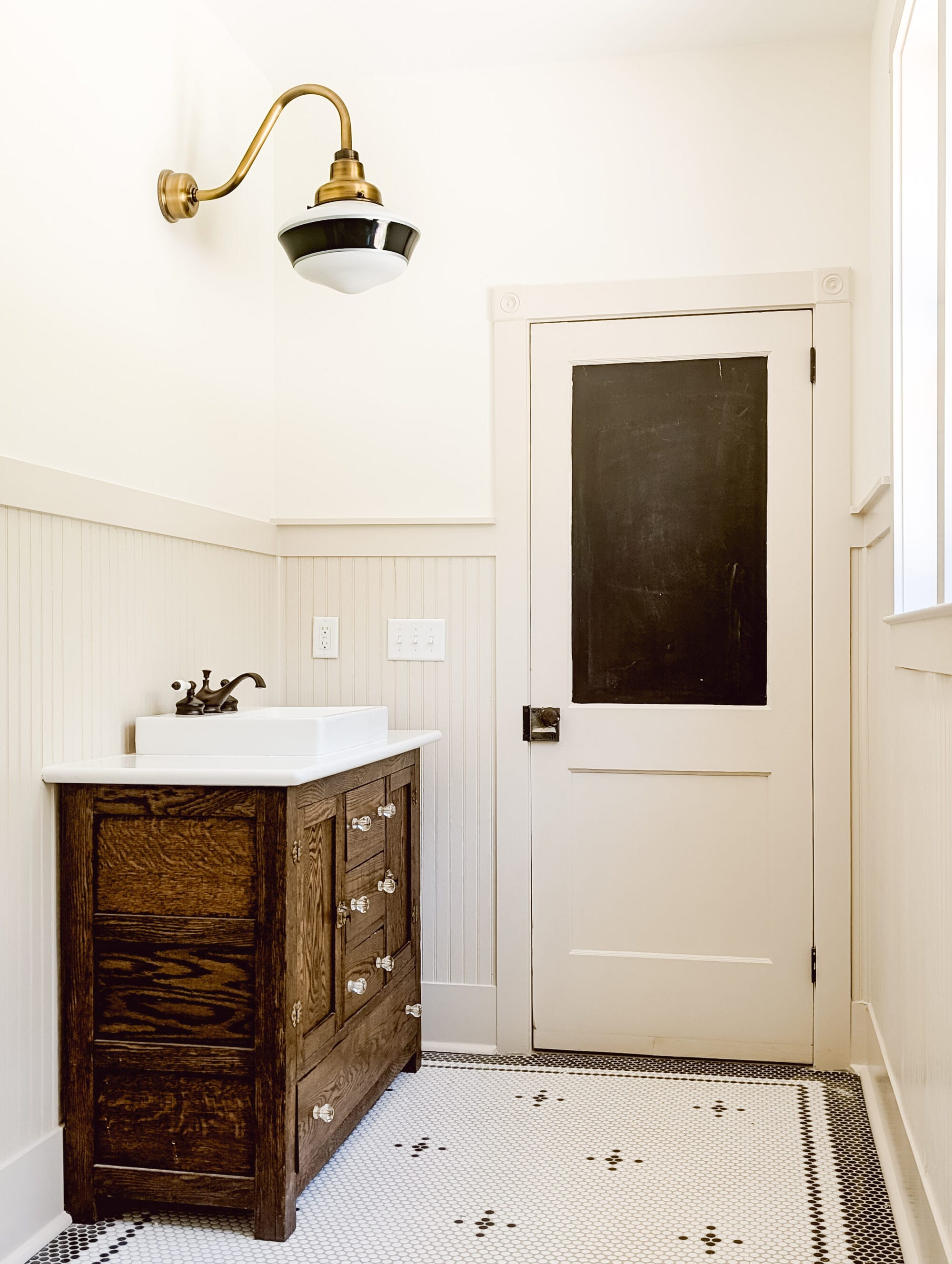 new old cottage bathroom with black and white details, white walls, tan beadboard paneling, and an antique bathroom vanity