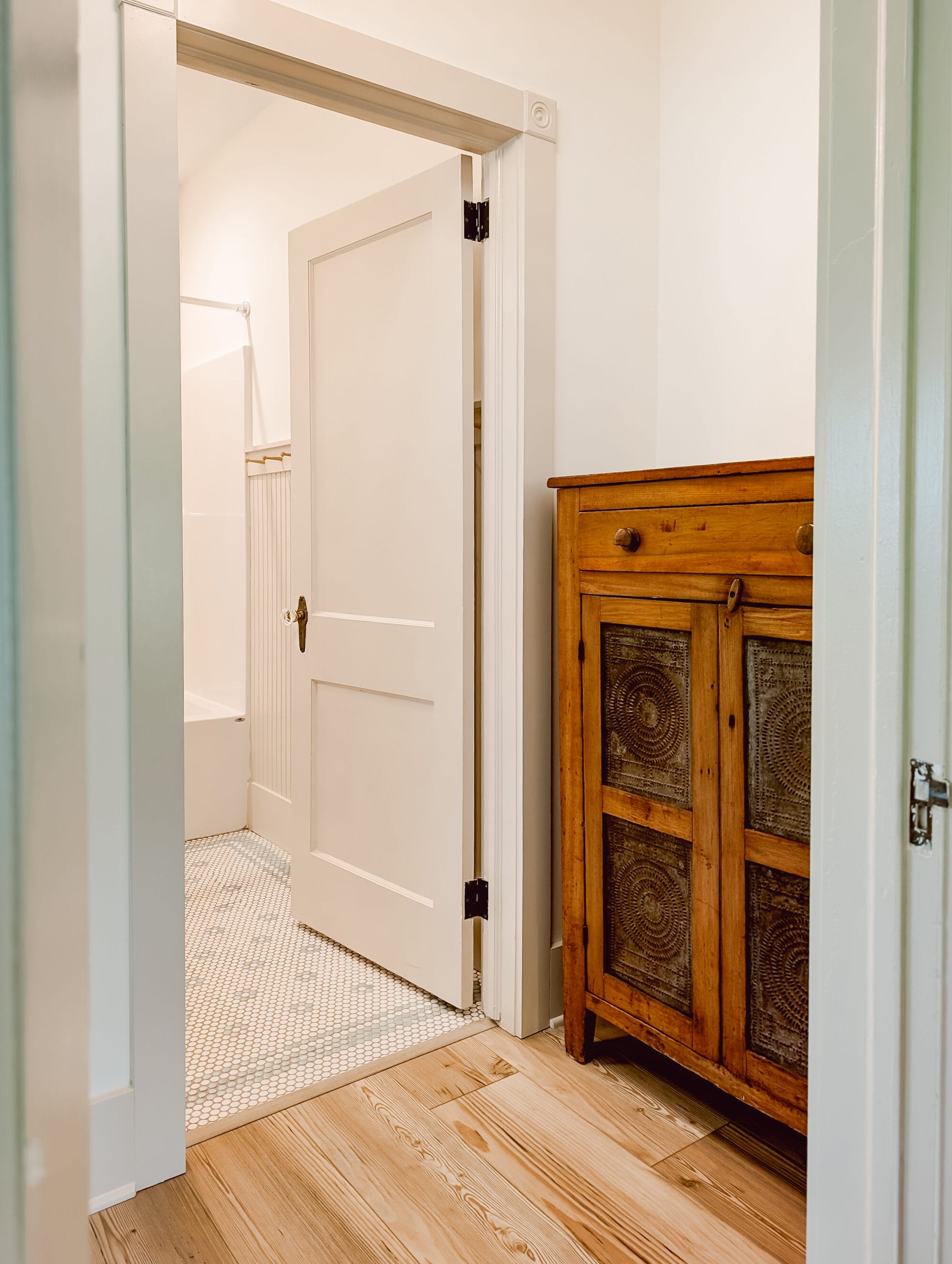 antique wood pie safe cabinet with punched tin design on the doors in the hallway next to the guest bathroom