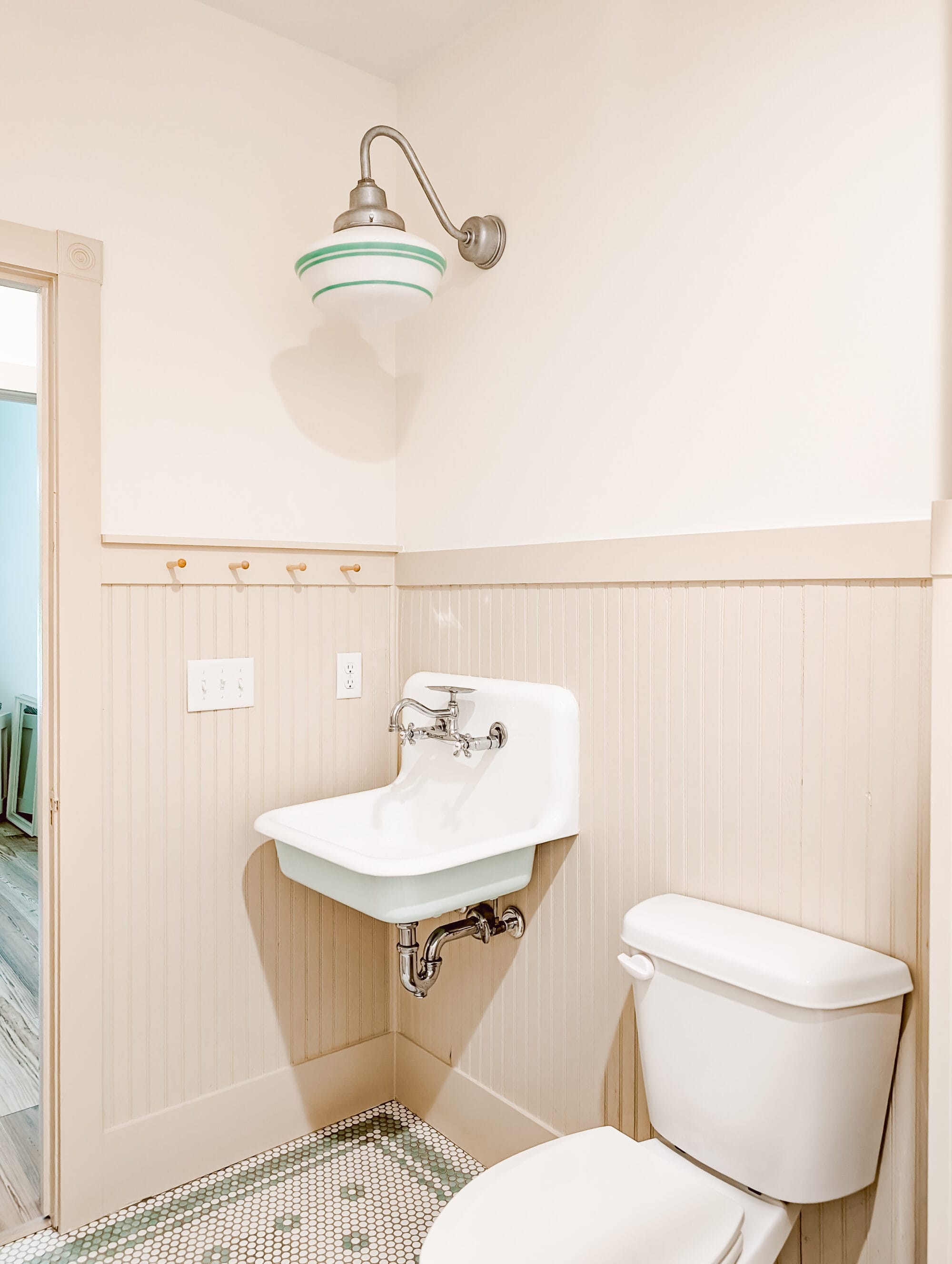 new old cottage bathroom with a vintage inspired schoolhouse light, an old fashioned wall mount sink, and penny tile floors