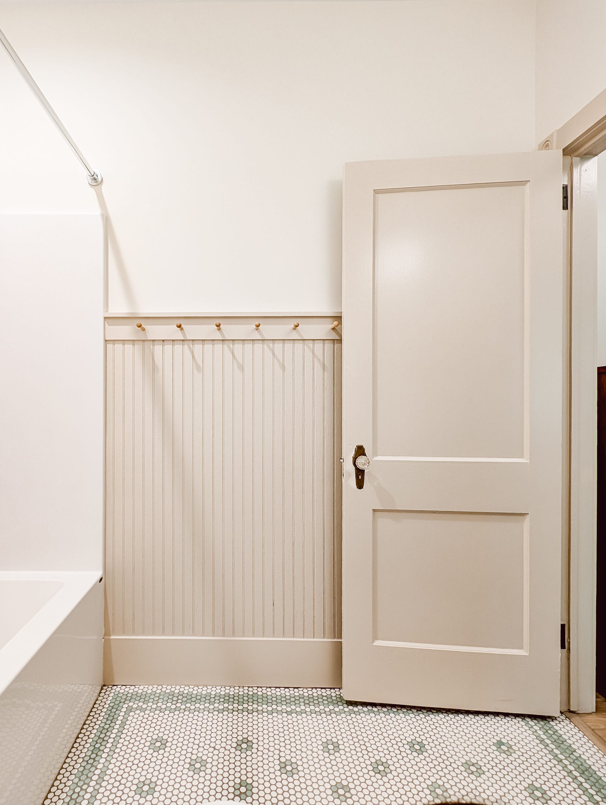 new old cottage bathroom with vintage inspired mint green and white penny tile floors in a daisy pattern, beadboard walls, peg hooks, and an antique door