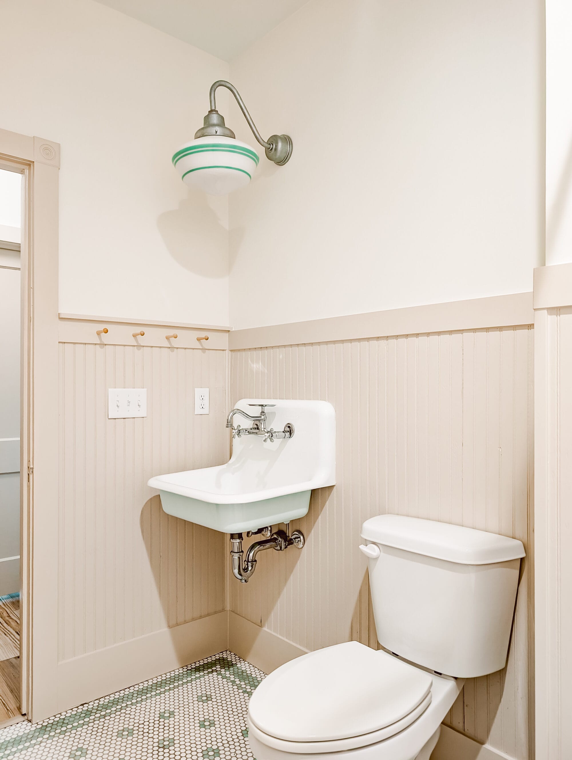 vintage inspired cottage bathroom with pops of mint green in the floors, the underside of the wall mount sink, and the schoolhouse light globe