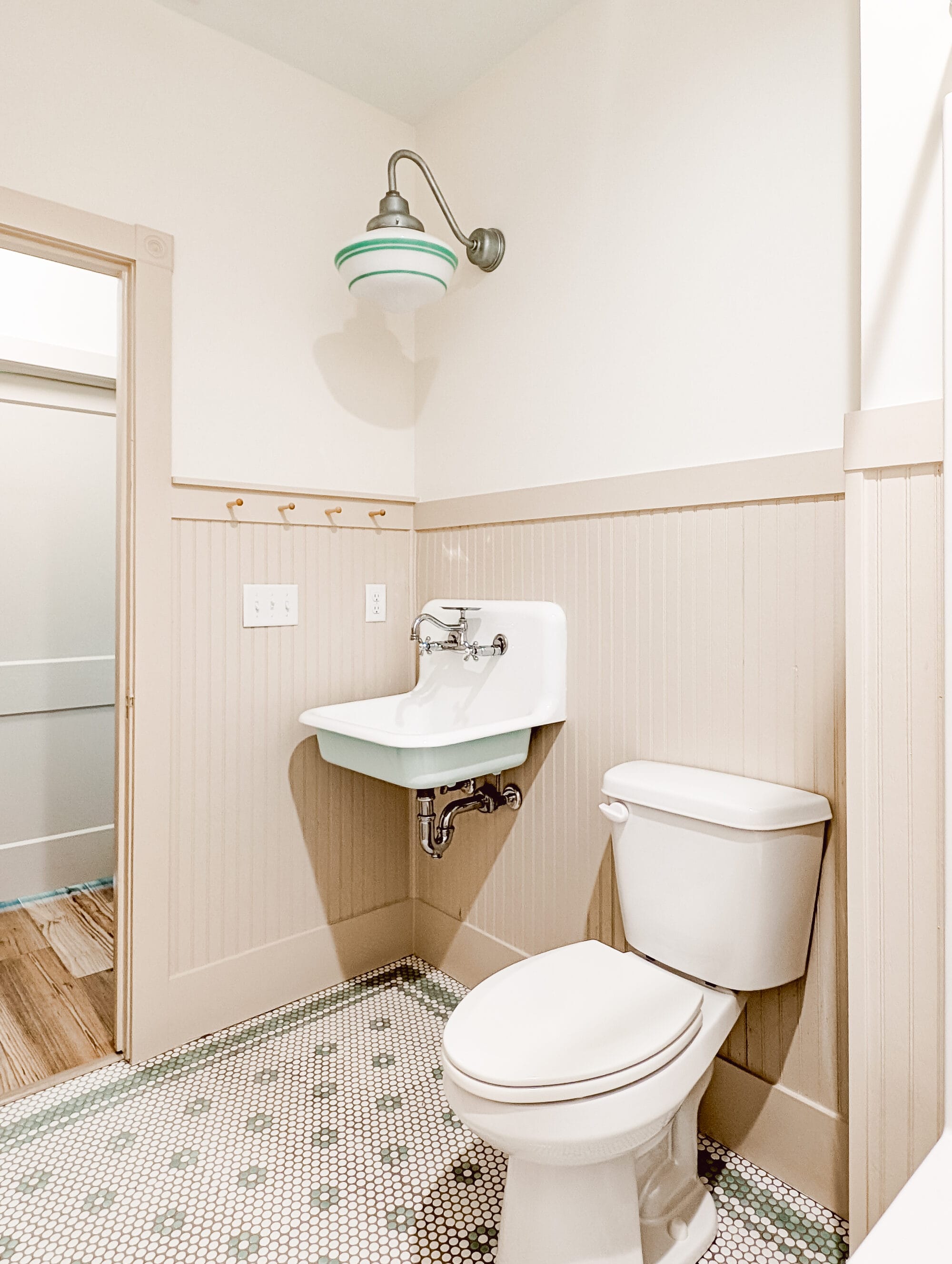 vintage cottage bathroom with white and tan walls, an old fashioned high back sink, and daisy penny tile floors