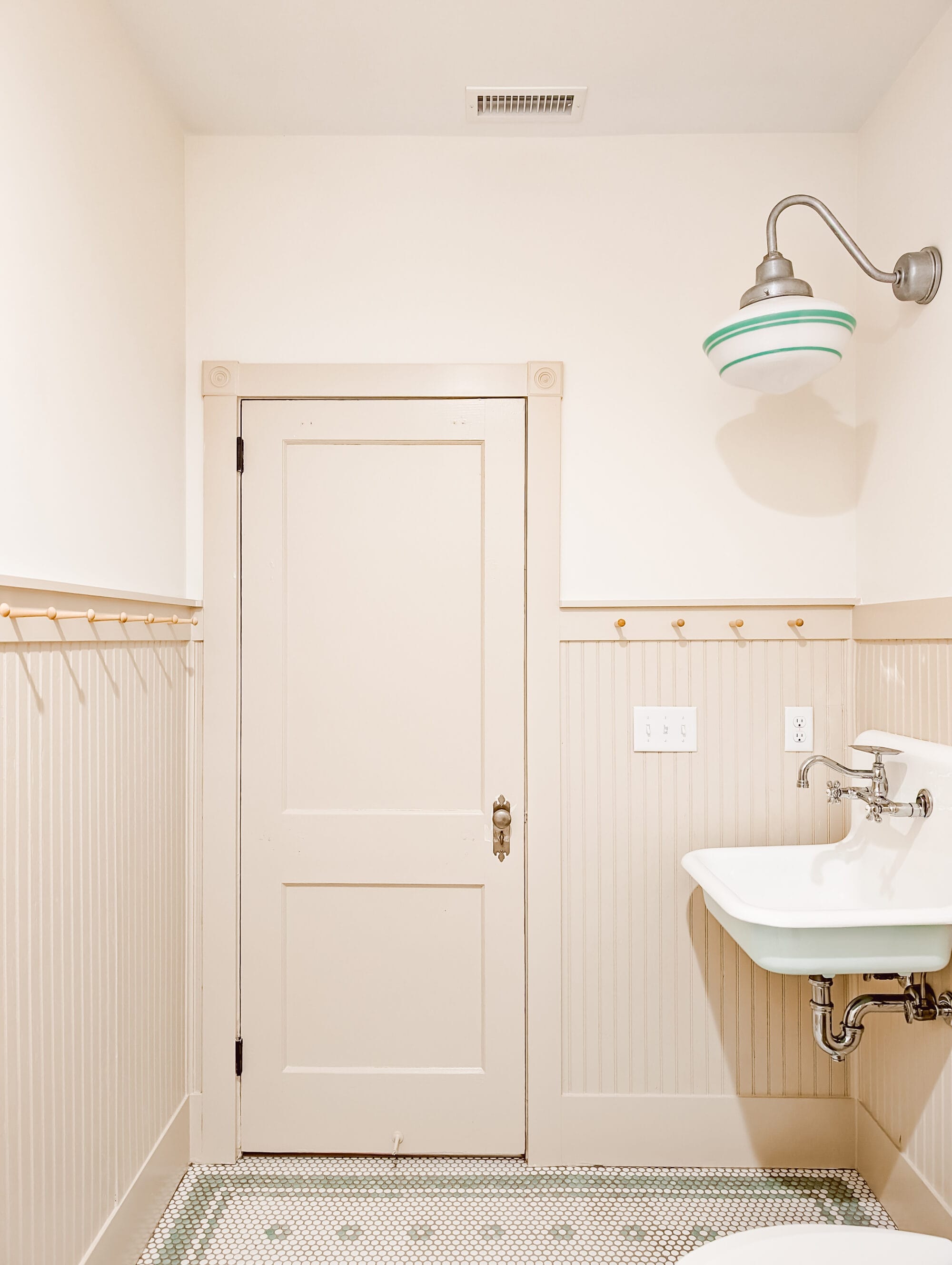 new old cottage bathroom with vintage inspired mint green and white penny tile floors in a daisy pattern, beadboard walls, peg hooks, and an antique door