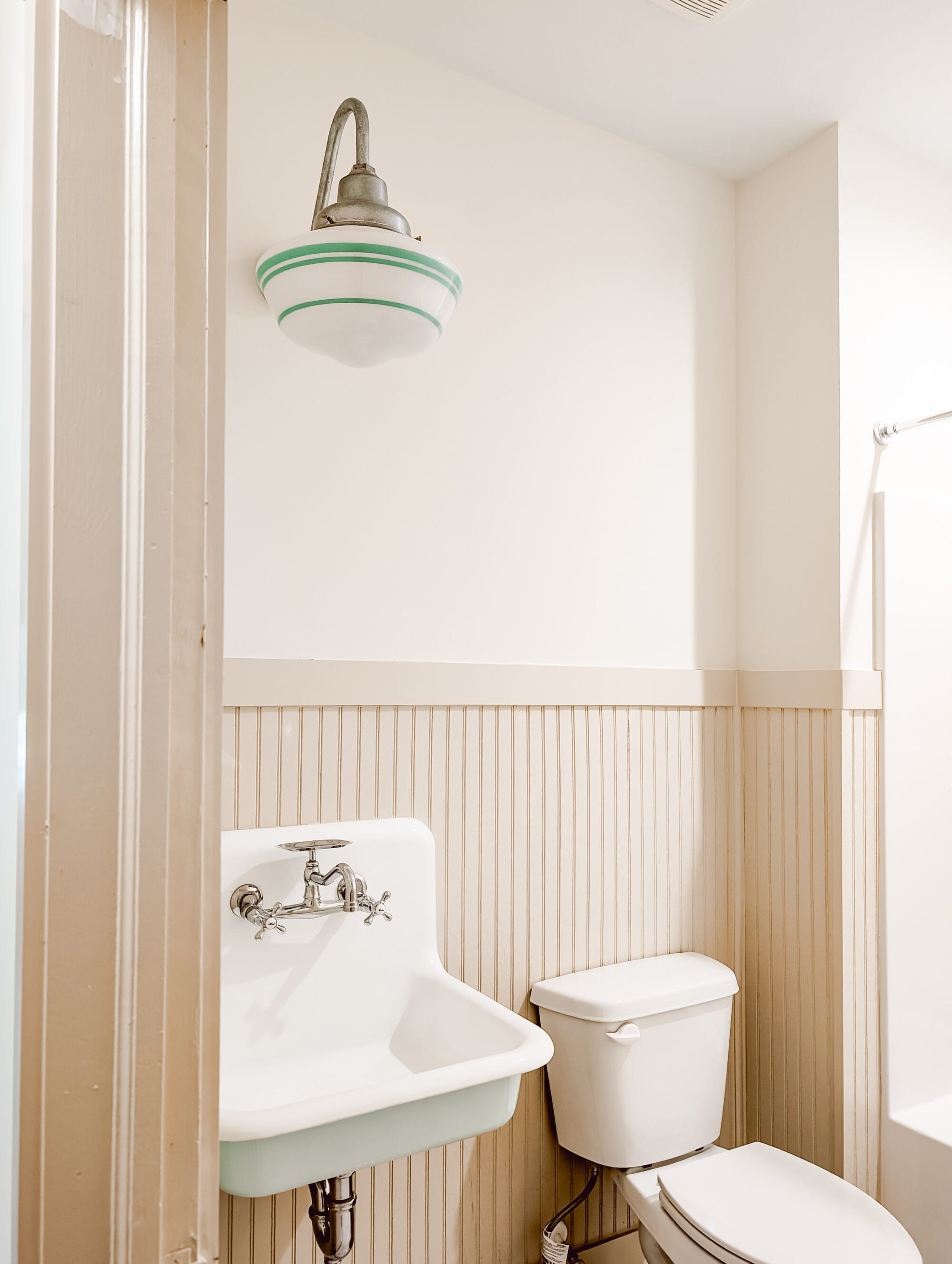 peeking into the guest bathroom at the vintage lighting and old fashioned sink mounted on a beadboard wall