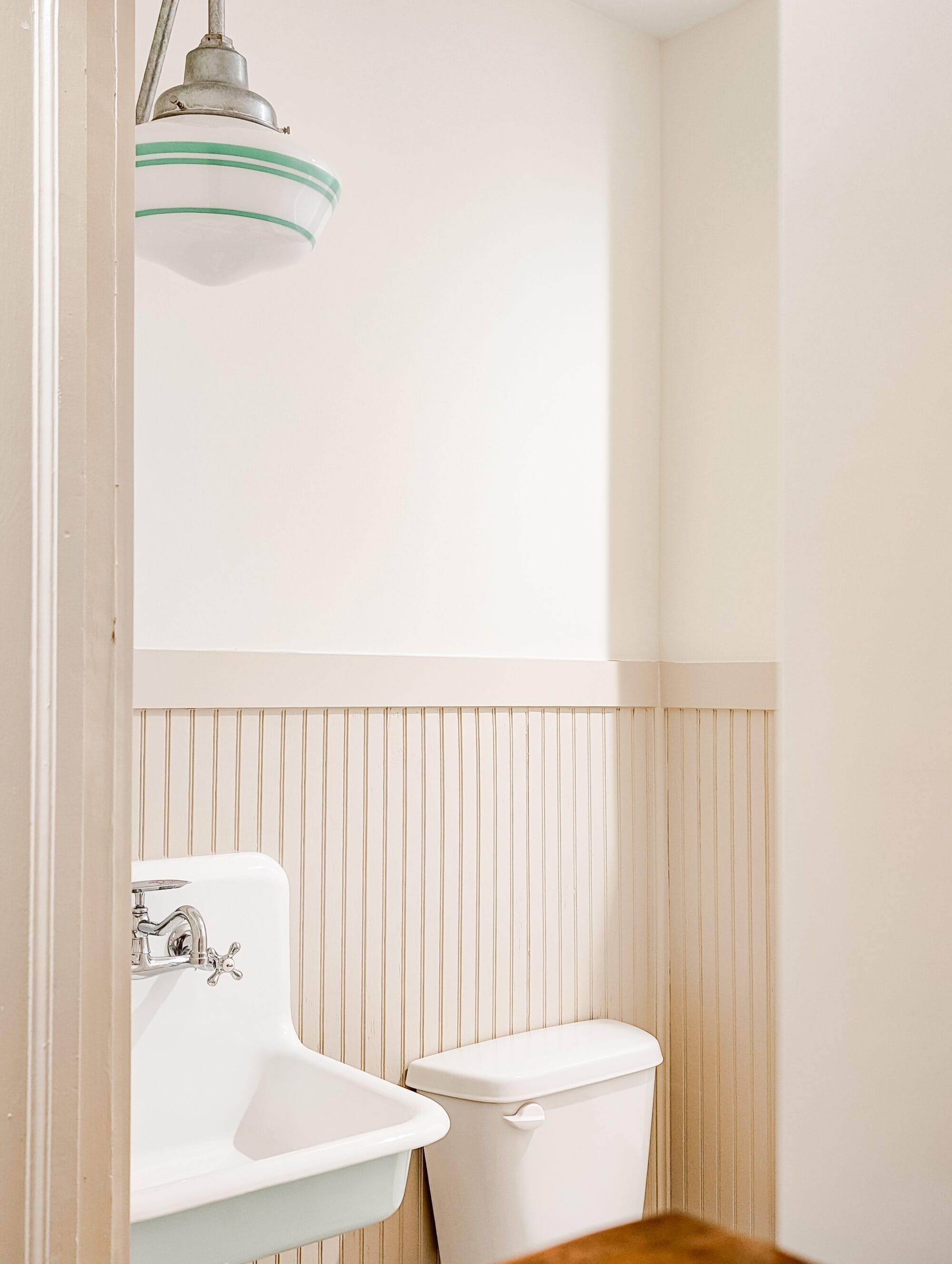 new old cottage bathroom with tan beadboard walls, a vintage schoolhouse light, and a wall mounted sink