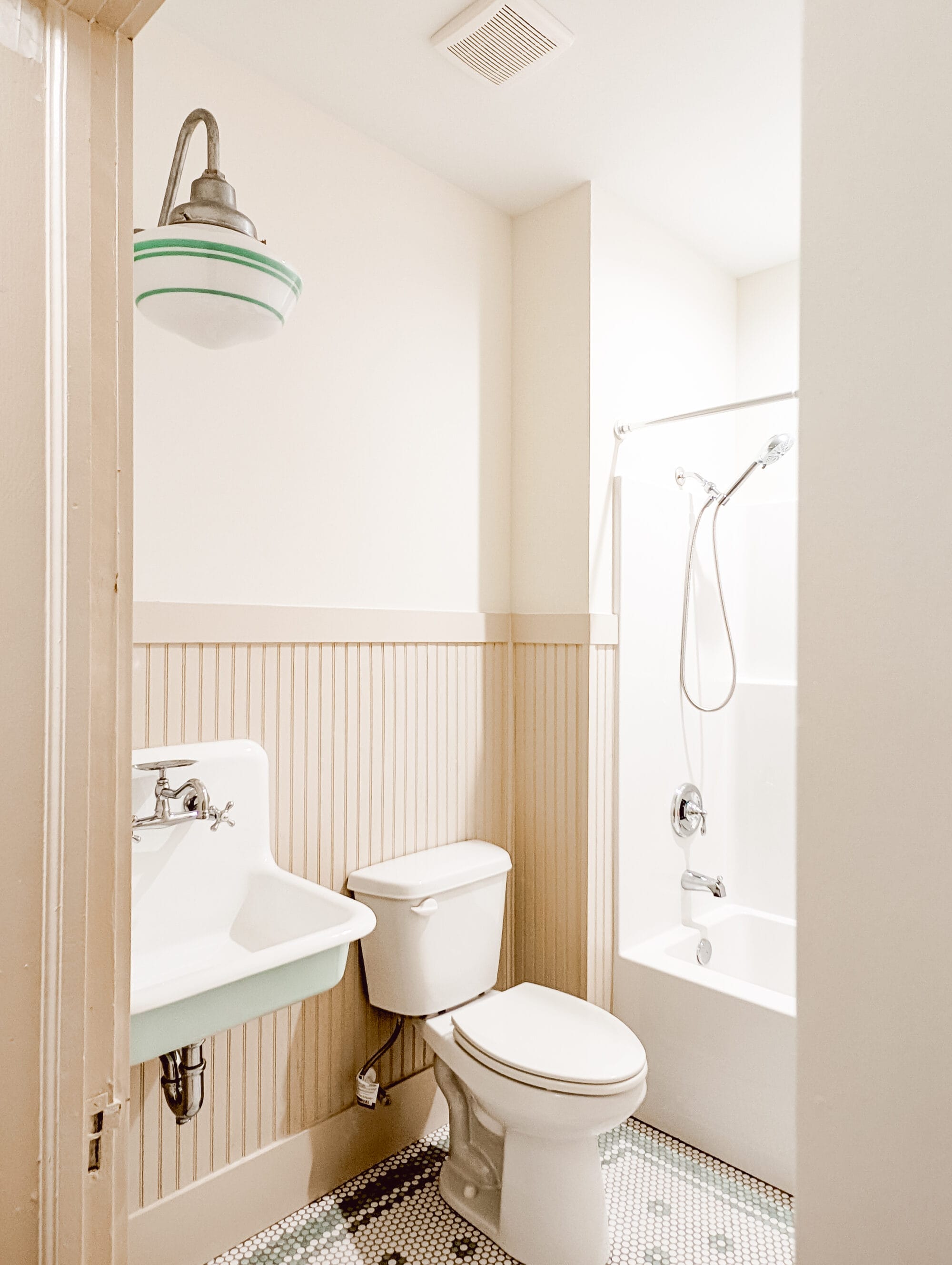 new old cottage bathroom with tan beadboard walls, a vintage schoolhouse light, and a wall mounted sink