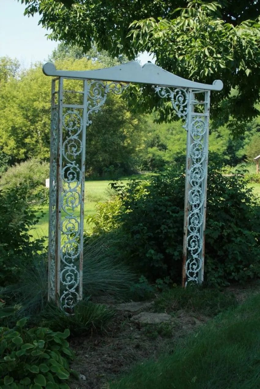eclectic garden arbor pieced together with two salvaged iron porch supports and a carved wood architectural piece at the top