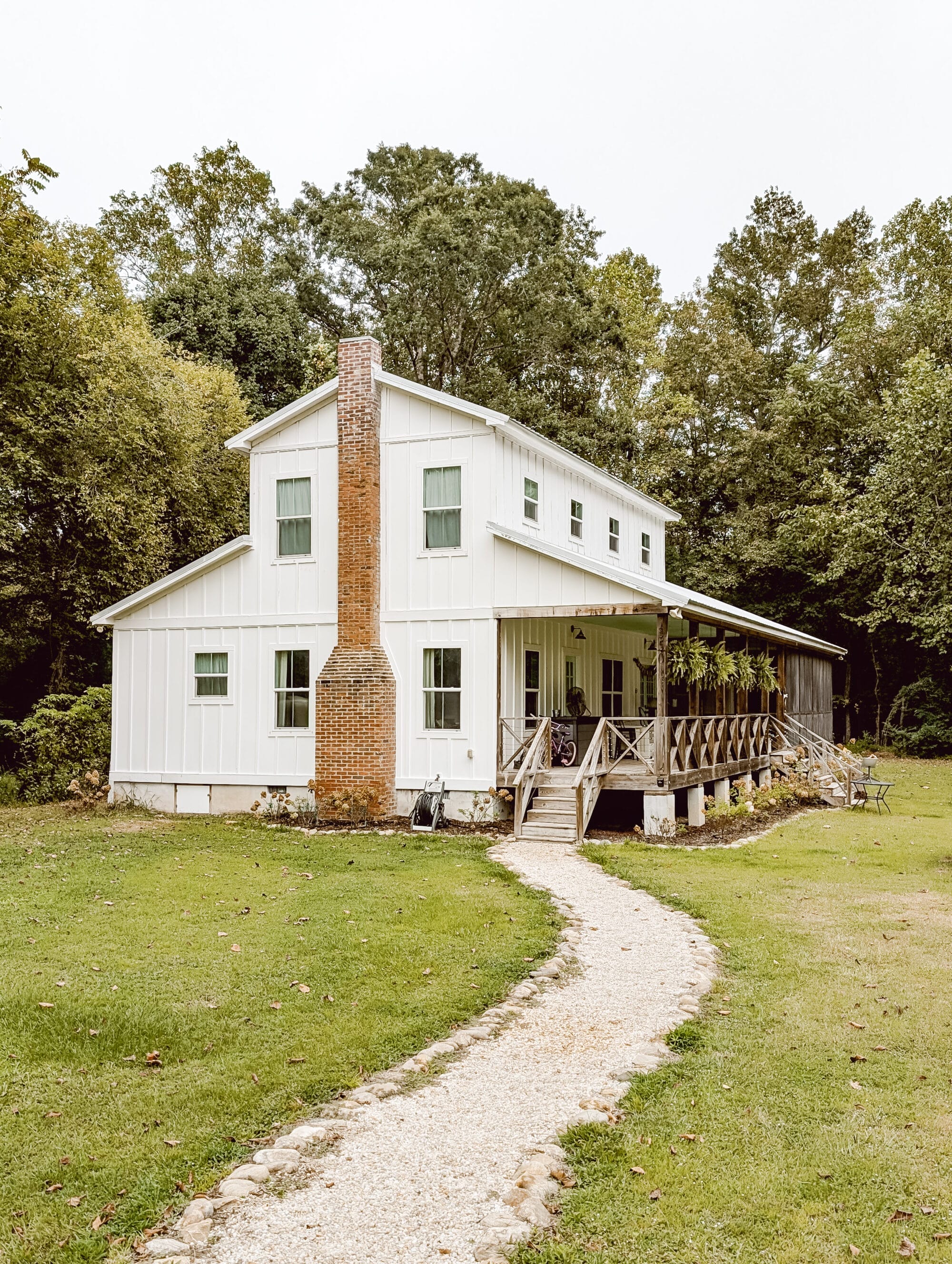 old white farmhouse with vertical siding, a red brick chimney, and a gravel path leading to the front porch