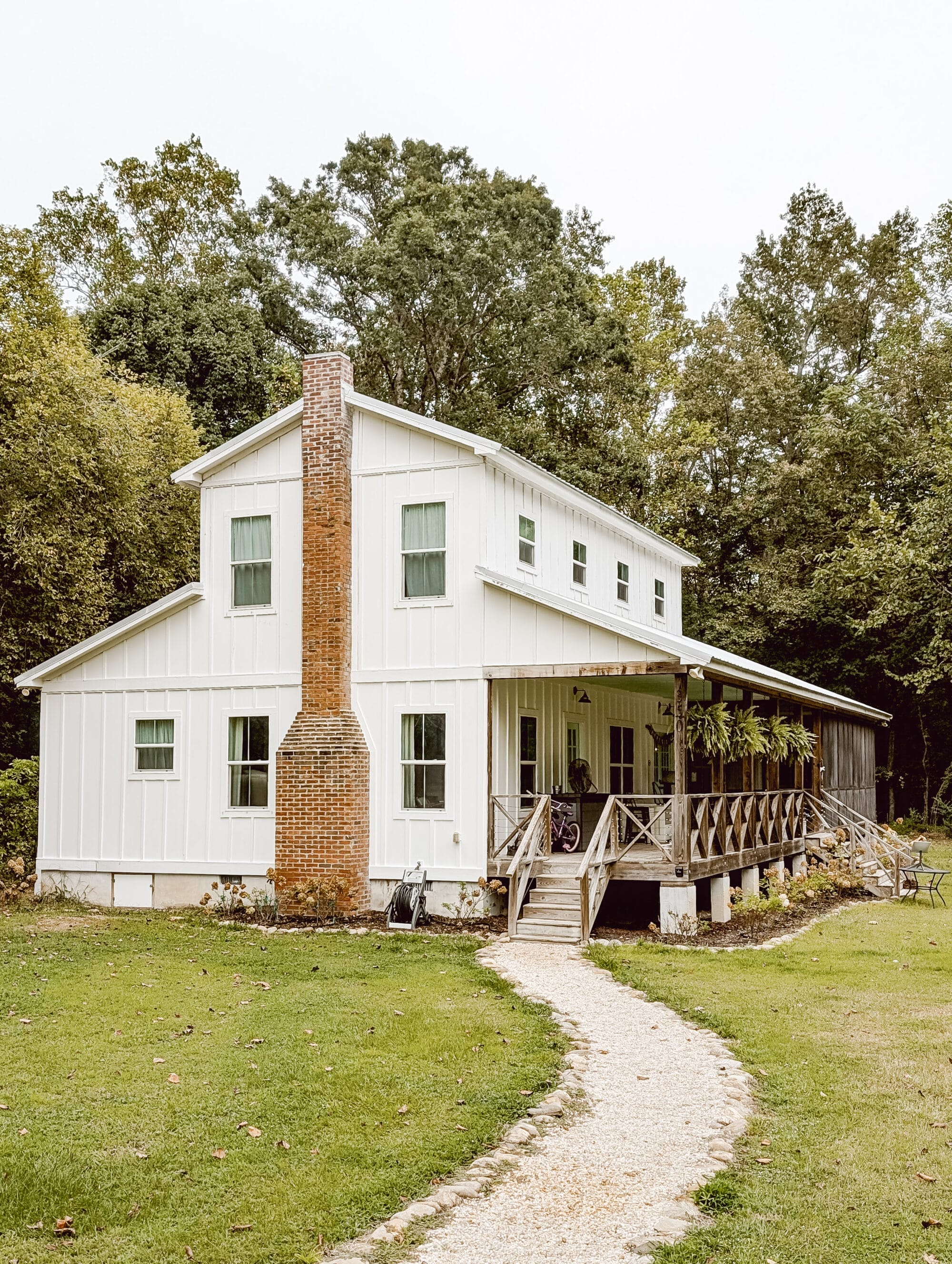 old white farmhouse with vertical siding, a red brick chimney, and a gravel path leading to the front porch