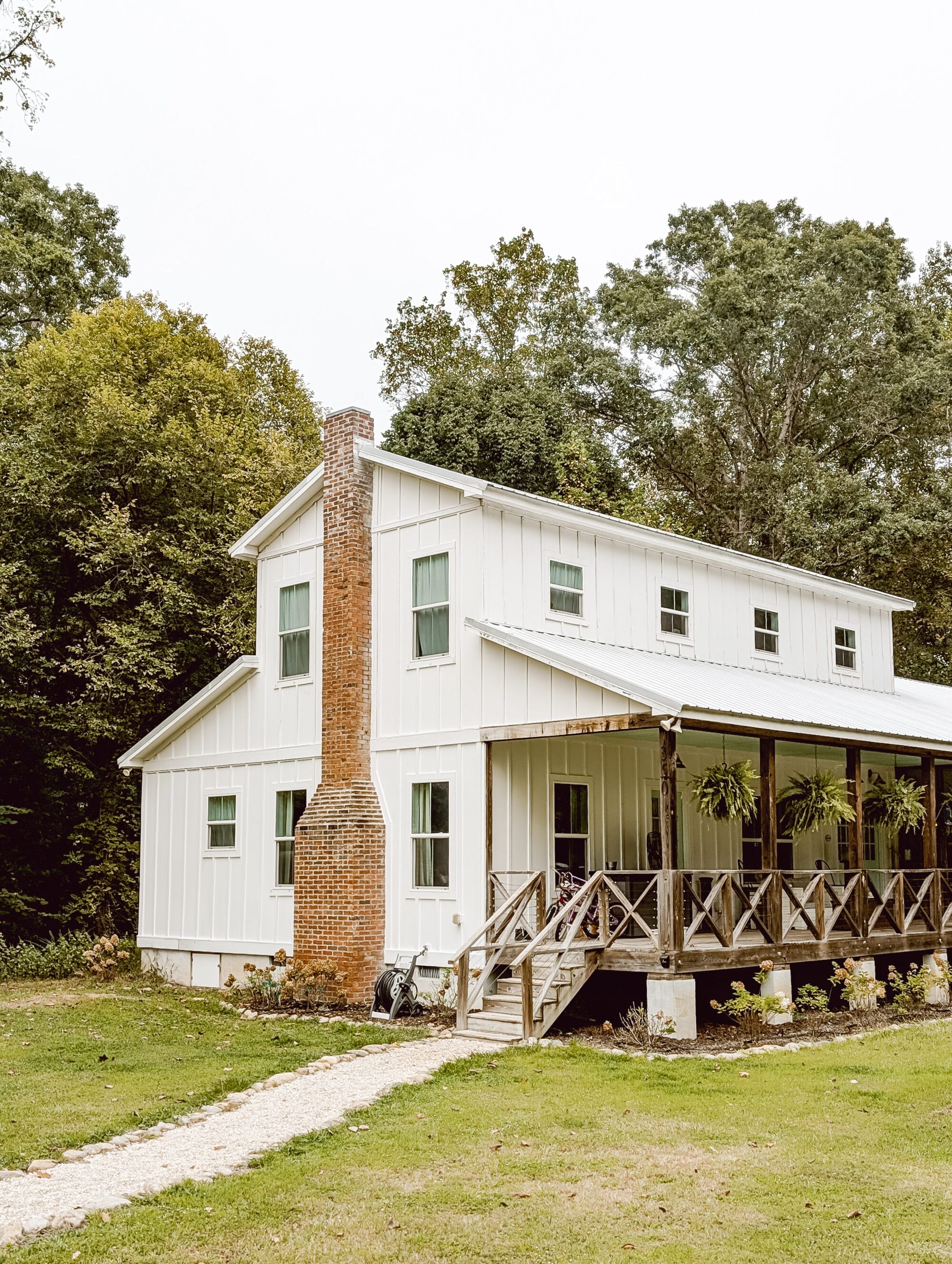 historic white 2-story farmhouse with board and batten siding, red brick chimney, and long front porch