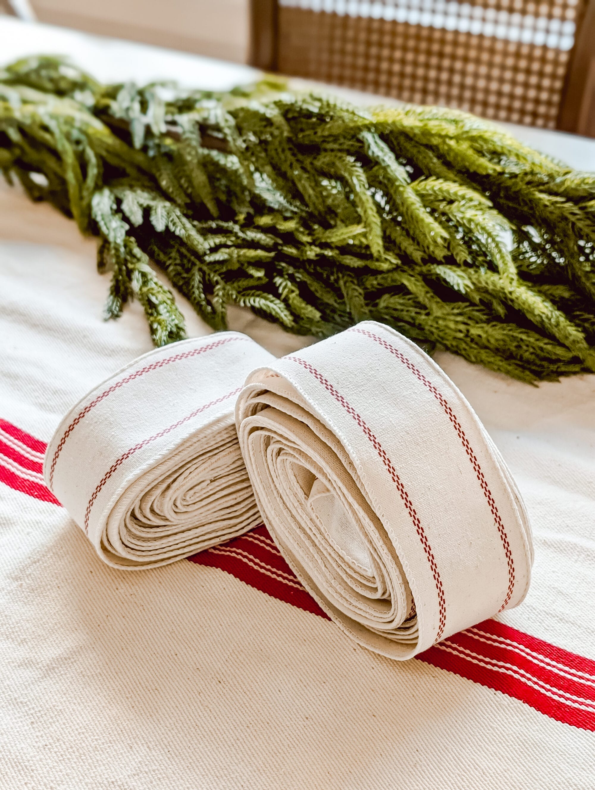 two rolls of wired grainsack ribbon with thin red striped, rolled and sitting on an antique red and white grainsack