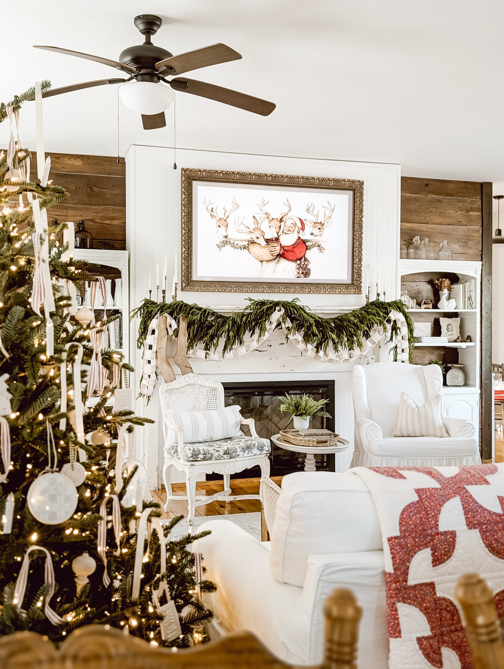 red and white quilt draped over white couch next to Christmas tree facing a white fireplace with antique mantel