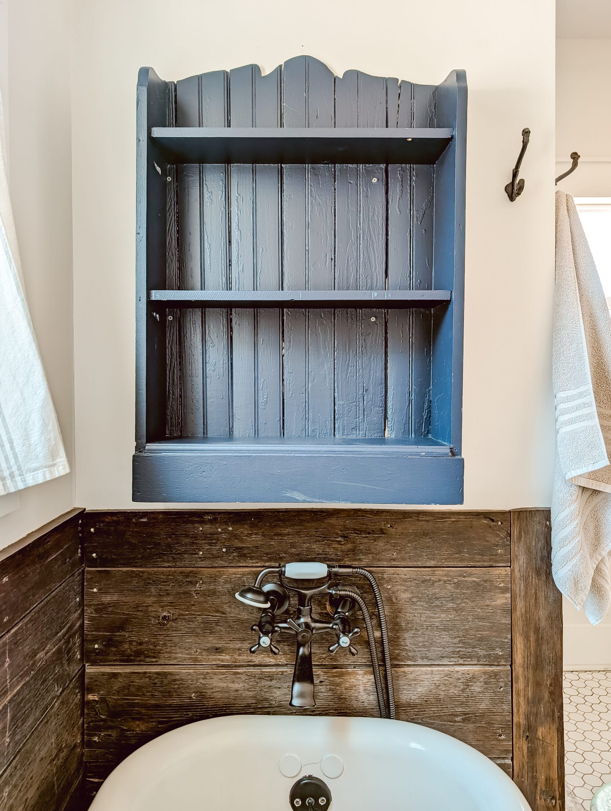 navy blue children's bookshelf hung up on the bathroom wall over the tub repurposed as decorative bathroom shelves