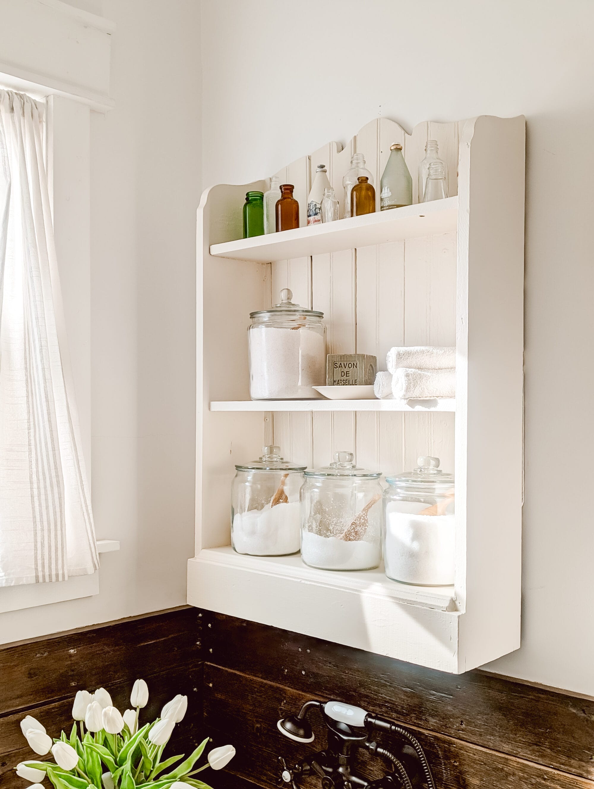 thrifted children's bookshelf hung up on the bathroom wall over the tub repurposed as decorative bathroom shelves