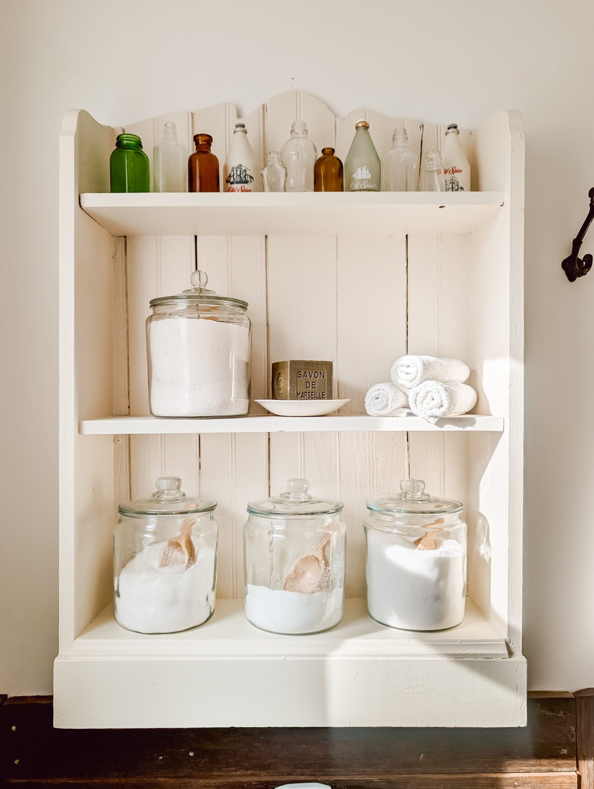 white painted bookshelf displaying small bottle collection and jars of bath salts